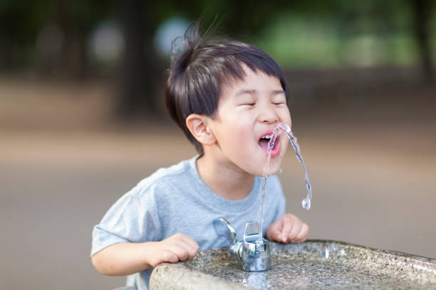 A Japanese boy is drinking water from a water fountain in a park