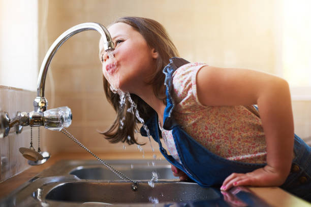 Shot of a little girl drinking water directly from the kitchen tap at home